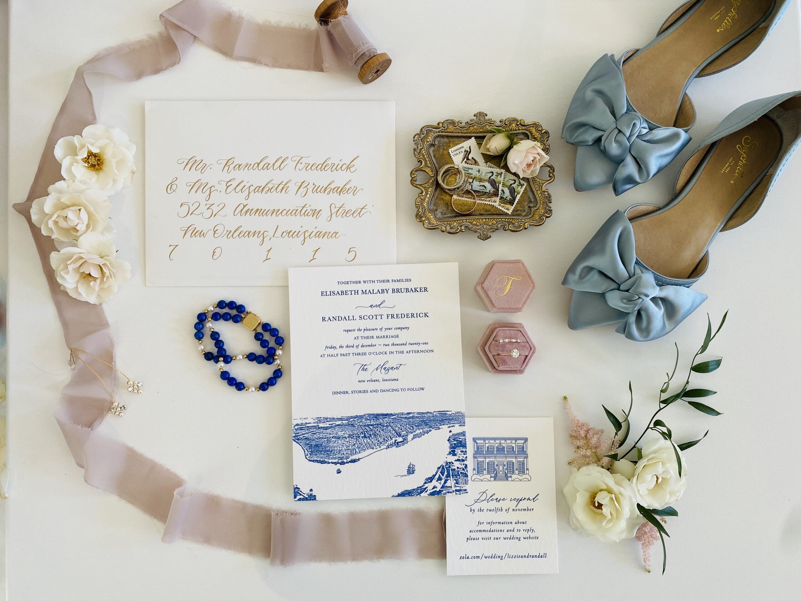Falt lay picture of wedding invitations, something blue shoes, rings, and details